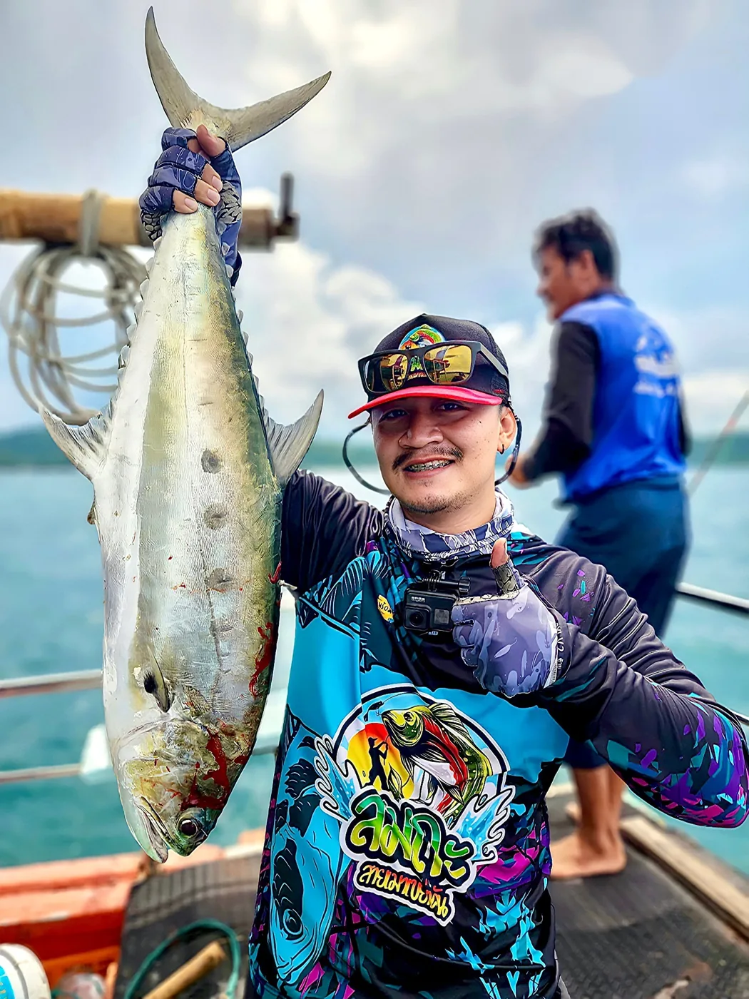 ลูกค้าสวมเสื้อตกปลาติดเบ็ดลายทีม ชูปลาตัวใหญ่บนเรือกลางทะเล